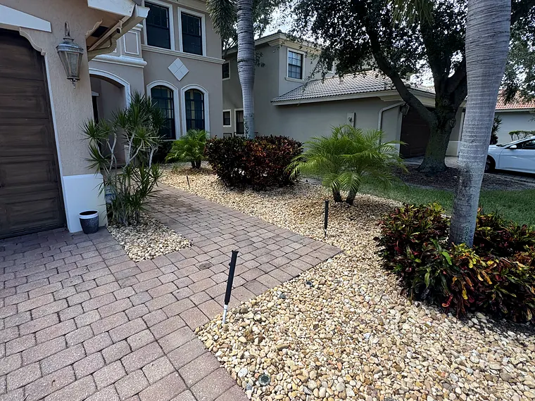 Paver walkway edged with river rock landscape beds and palms