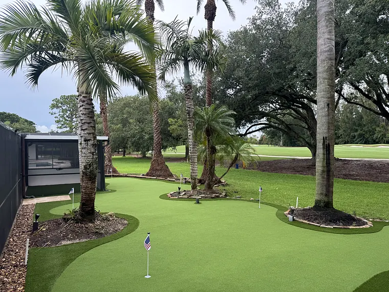 Backyard artificial turf putting green with palms and planted beds